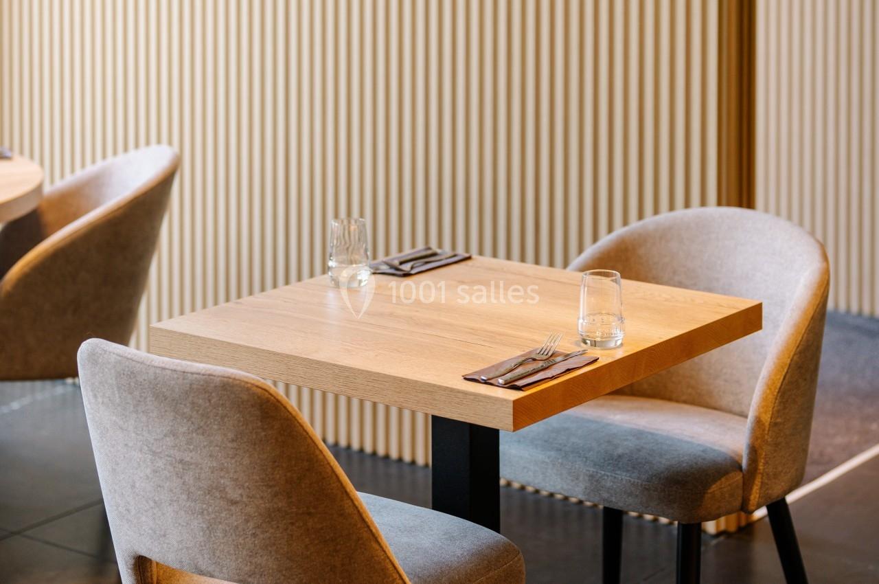 Table en bois pour deux personnes avec chaises rembourrées, dressée avec couverts et verres, dans un intérieur moderne.
