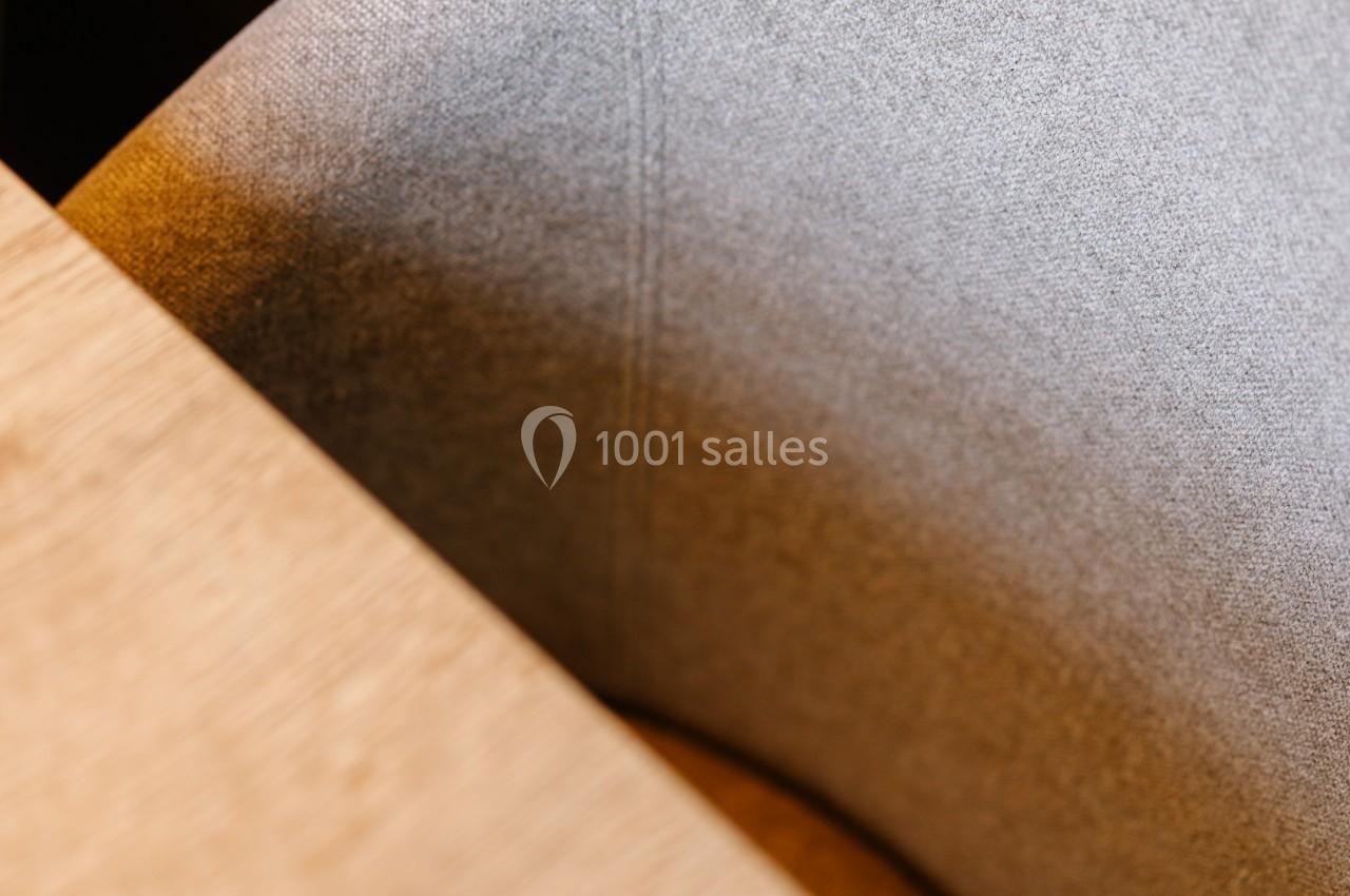 Chaise en tissu gris clair partiellement visible près d'une table en bois clair, éclairée par une lumière douce.
