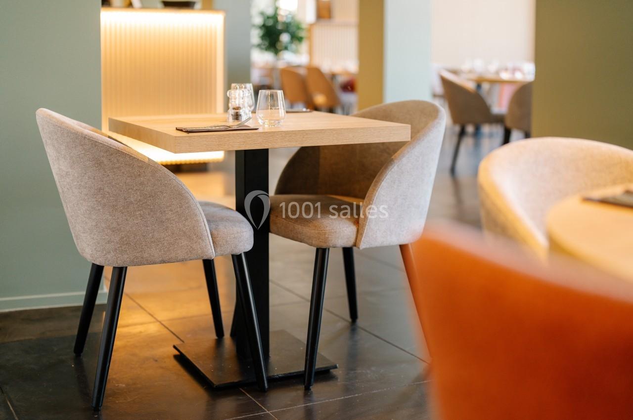 Table en bois avec deux chaises rembourrées dans un restaurant lumineux au sol en carrelage foncé.
