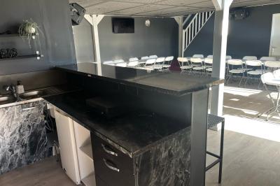 Terrasse extérieure avec pergola en bois, tables, chaises, oliviers et chemin en bois sur gazon et gravier.