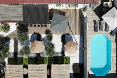 Terrasse extérieure avec pergola en bois, tables, chaises, oliviers et chemin en bois sur gazon et gravier.