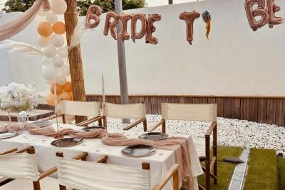Terrasse extérieure avec pergola en bois, tables, chaises, oliviers et chemin en bois sur gazon et gravier.