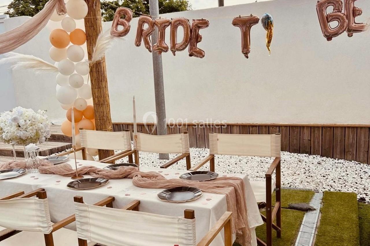Table décorée pour une fête avec des ballons, une guirlande ’Bride to Be’ et des chaises blanches en extérieur.