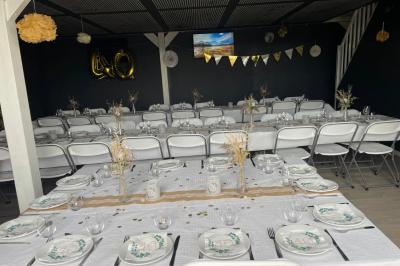 Terrasse extérieure avec pergola en bois, tables, chaises, oliviers et chemin en bois sur gazon et gravier.