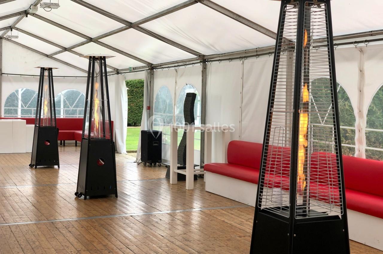 Chauffages de terrasse à gaz allumés dans une tente aménagée avec des bancs rouges et un sol en bois.