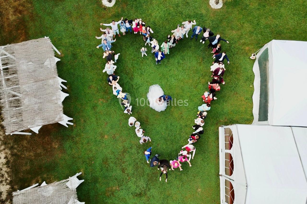 Vue aérienne d'un groupe de personnes formant un cœur autour d'un couple en tenue de mariage sur une pelouse.