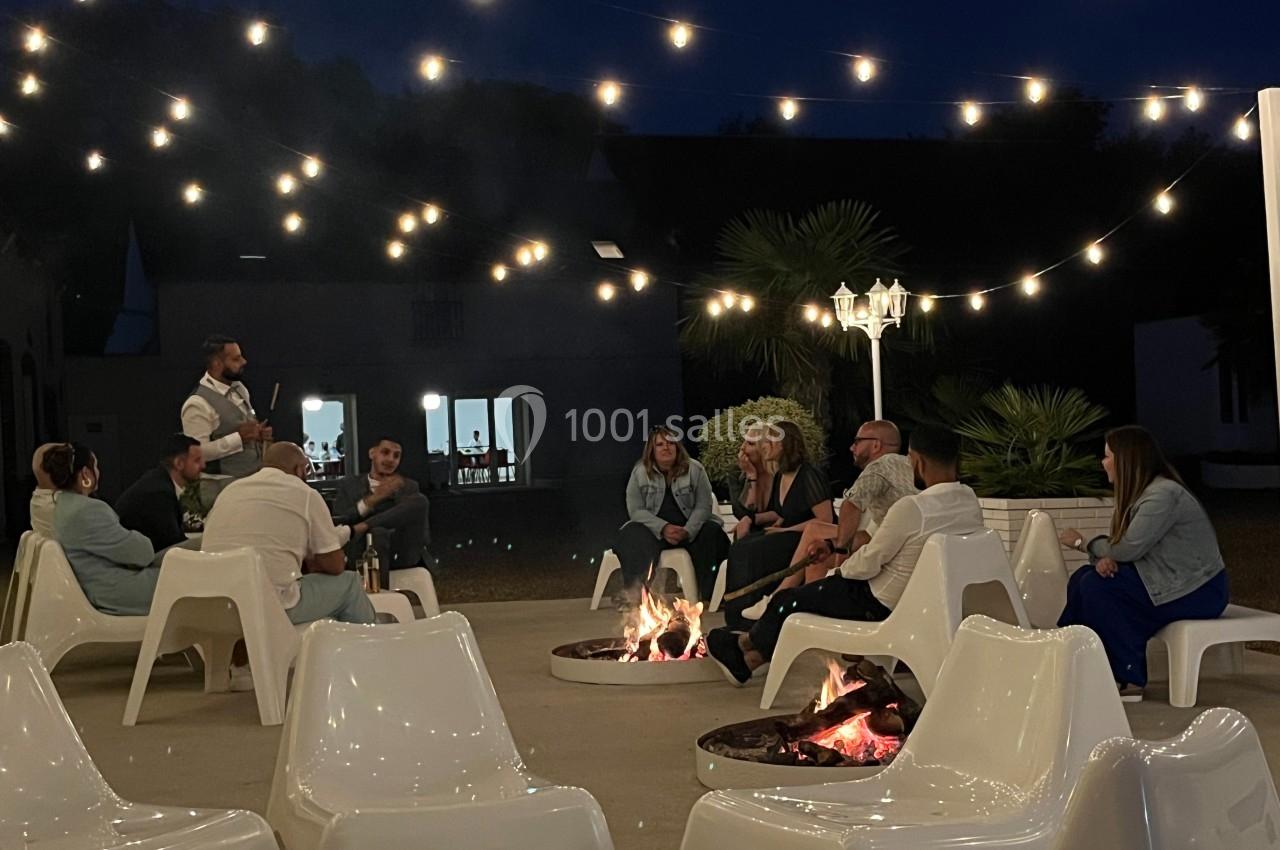 Un groupe de personnes assises autour de braseros allumés, sous des guirlandes lumineuses, en soirée.