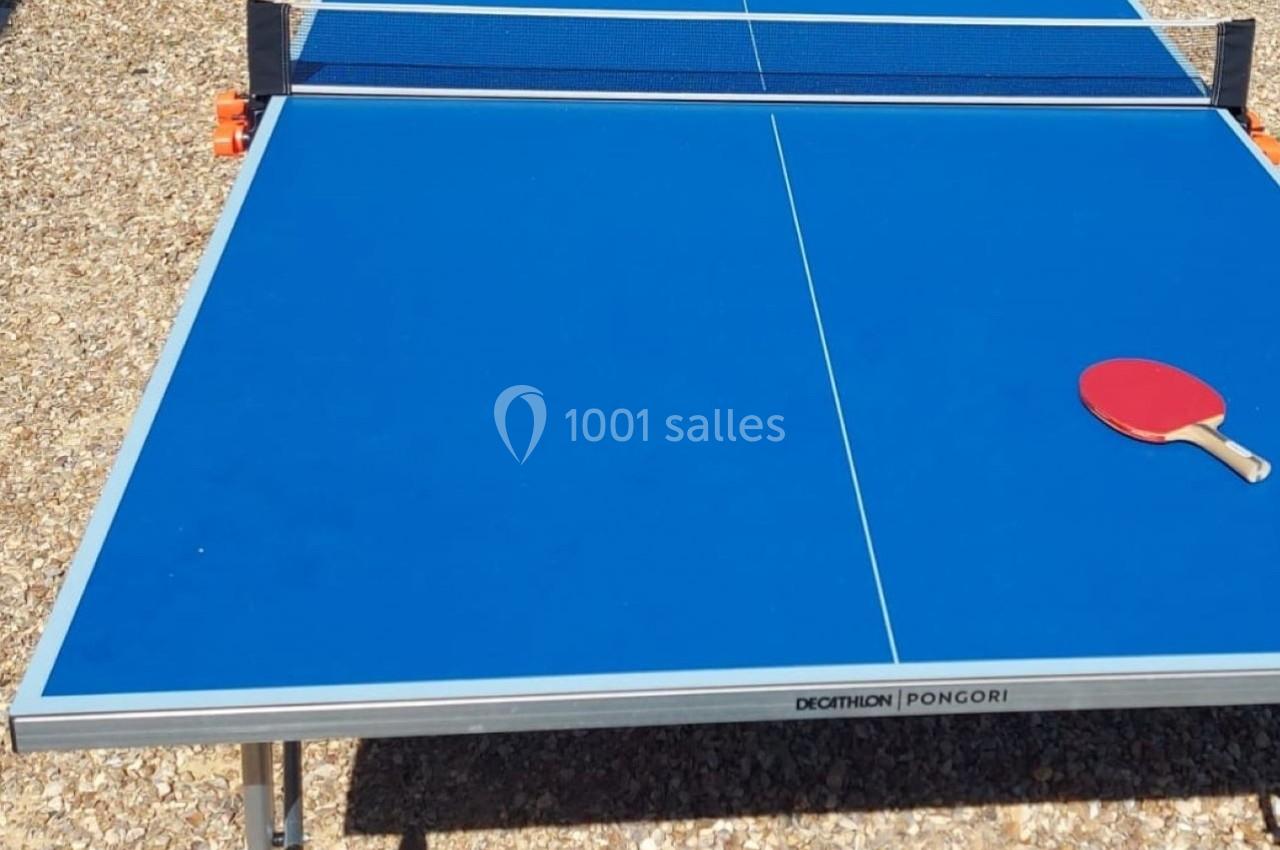 Table de tennis de table bleue en extérieur, avec deux raquettes rouges posées de part et d'autre du filet.