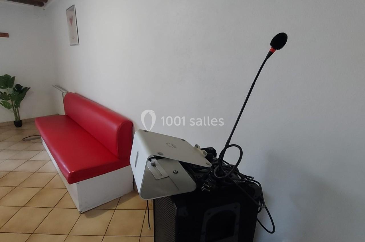 Un canapé rouge contre un mur blanc, à côté d'un haut-parleur avec un micro et un projecteur posé dessus.