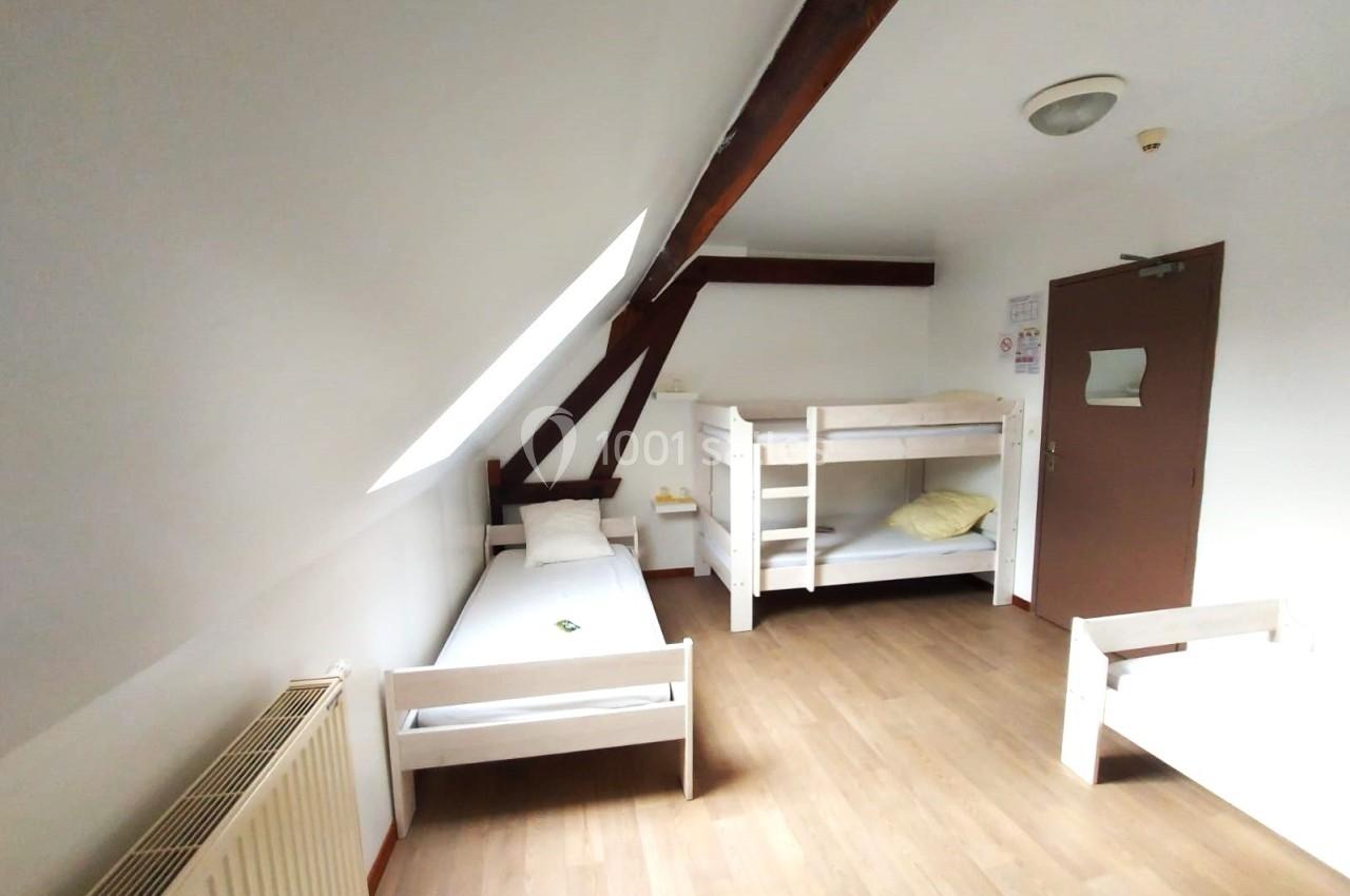 Chambre simple avec lits superposés et lit individuel, parquet au sol, murs blancs et poutre apparente.