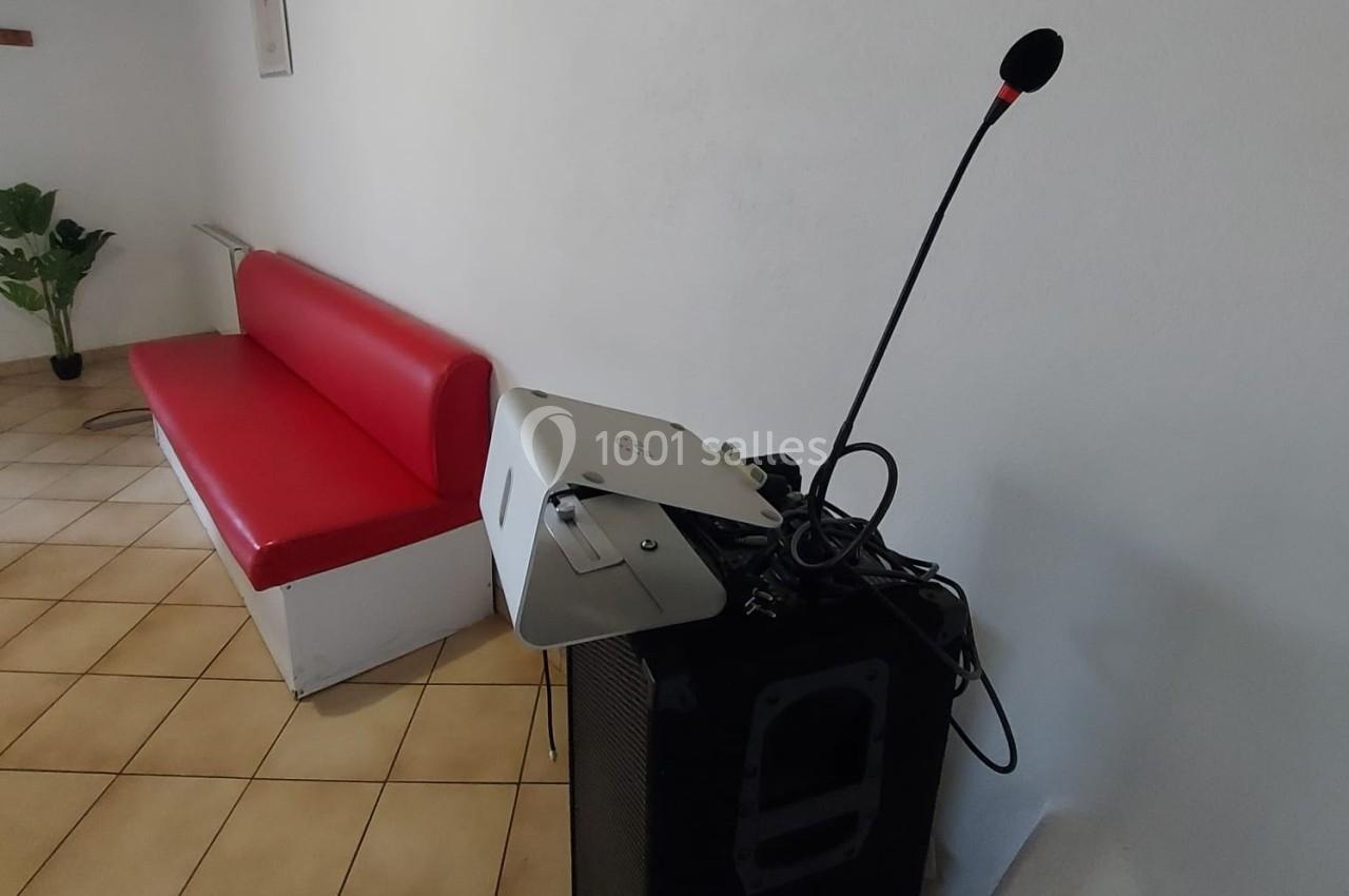 Un micro sur pied et un projecteur posés sur une enceinte, près d'une banquette rouge dans une pièce carrelée.