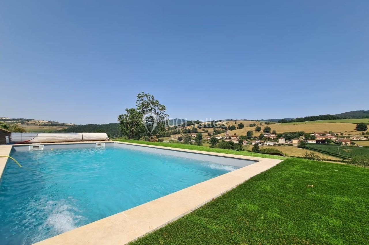 Piscine extérieure entourée de pelouse avec vue sur une campagne vallonnée sous un ciel dégagé.