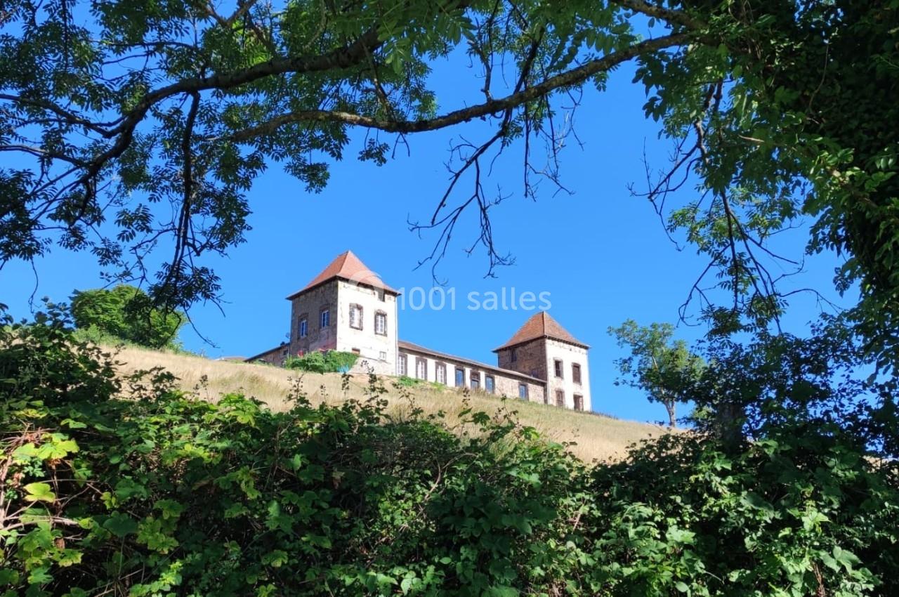Vue d'un bâtiment à deux tours avec toits rouges, entouré de végétation et ciel bleu en arrière-plan.
