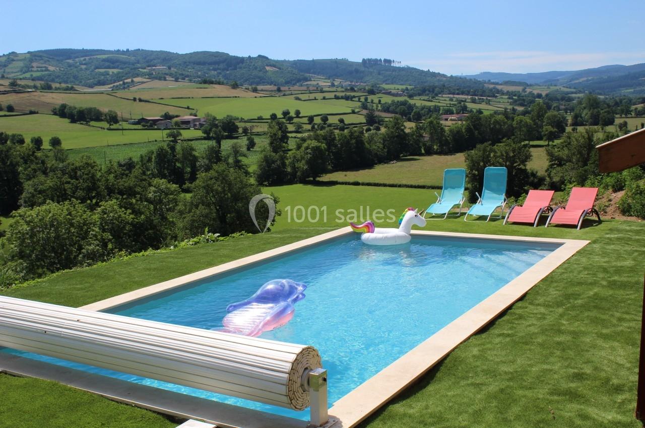 Piscine extérieure avec jouets gonflables, entourée de chaises longues colorées et vue sur une campagne vallonnée.