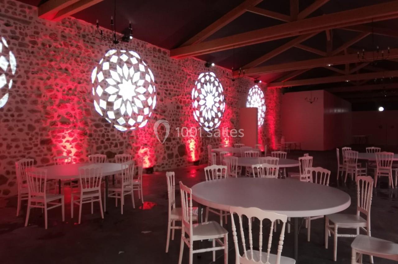 Salle décorée avec des tables rondes, chaises blanches et éclairage rouge, ornée de motifs lumineux sur les murs en pierre.