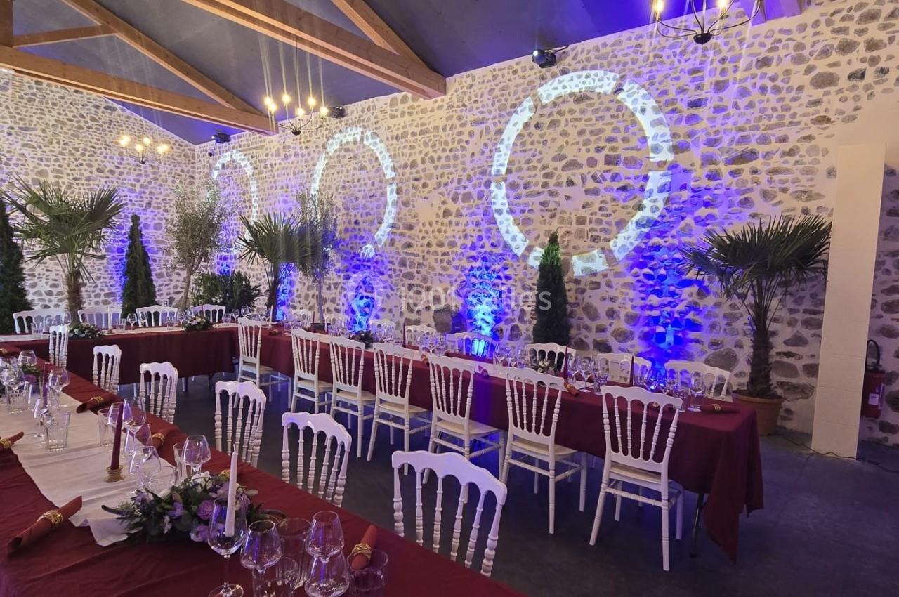 Salle de réception en pierre avec tables dressées, nappes bordeaux et éclairages colorés projetés sur les murs.