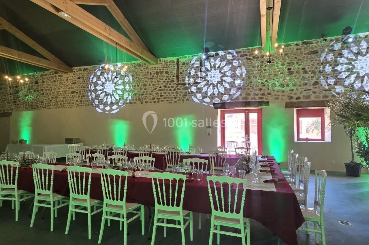 Salle de réception décorée avec des tables dressées, éclairages verts et projections lumineuses sur les murs en pierre.