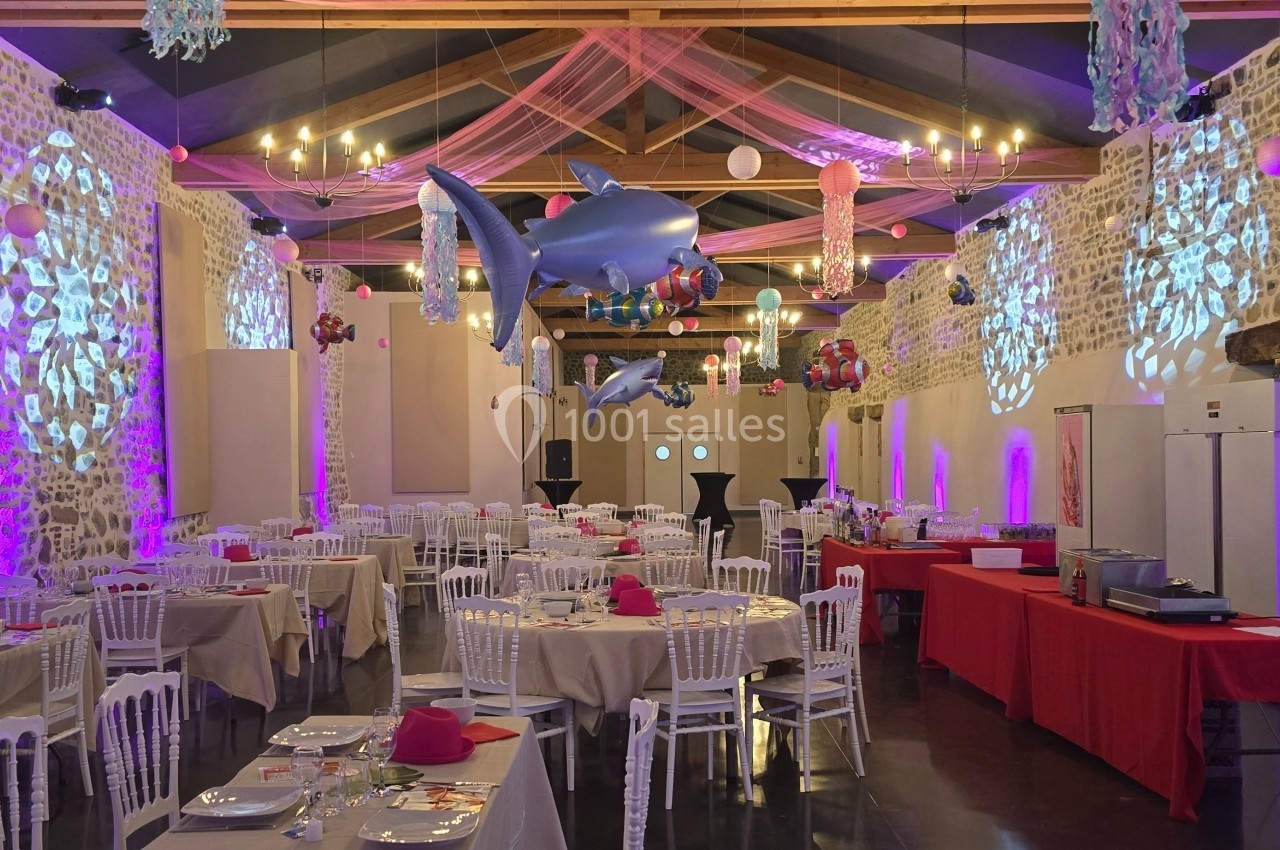 Salle de réception décorée avec des nappes rouges, des tables dressées et des ballons suspendus en forme d'animaux marins.