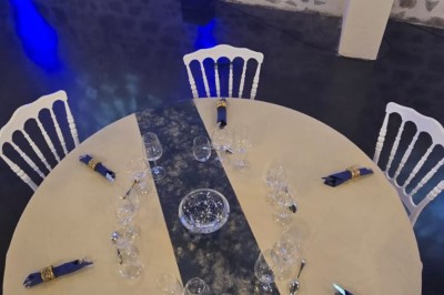 Grande paella servie dans un plat rond au premier plan, avec des convives attablés dans une salle de réception décorée.