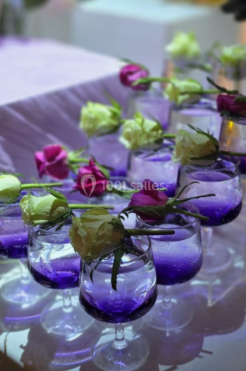 Verres remplis de liquide violet décorés de roses blanches et roses, disposés sur une table.