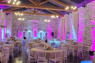 Grande paella servie dans un plat rond au premier plan, avec des convives attablés dans une salle de réception décorée.