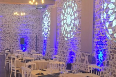 Grande paella servie dans un plat rond au premier plan, avec des convives attablés dans une salle de réception décorée.