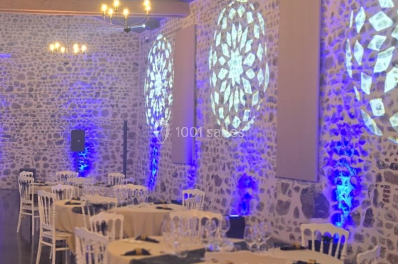 Salle en pierre décorée pour un événement, avec tables dressées, éclairage bleu et projections lumineuses sur les murs.