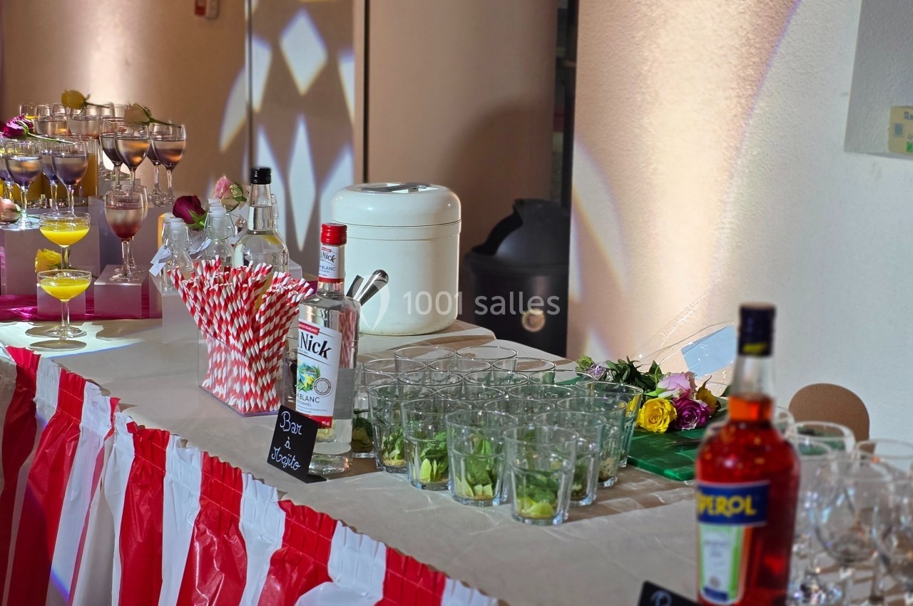 Table de buffet avec boissons alcoolisées et non alcoolisées, verres, pailles et décorations colorées.