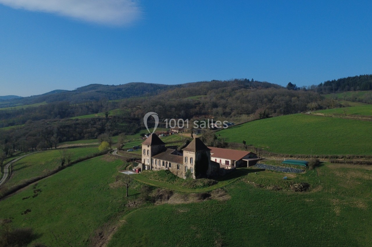 Vue aérienne d'un bâtiment historique entouré de collines verdoyantes sous un ciel bleu dégagé.
