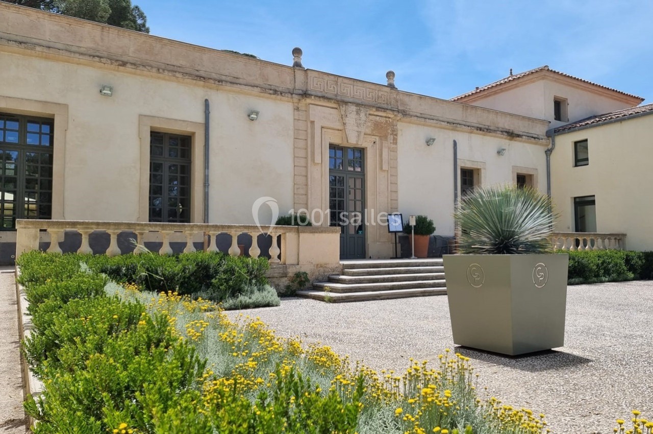 Façade d'un bâtiment ancien avec des escaliers, des plantes en pot et un parterre fleuri au premier plan.
