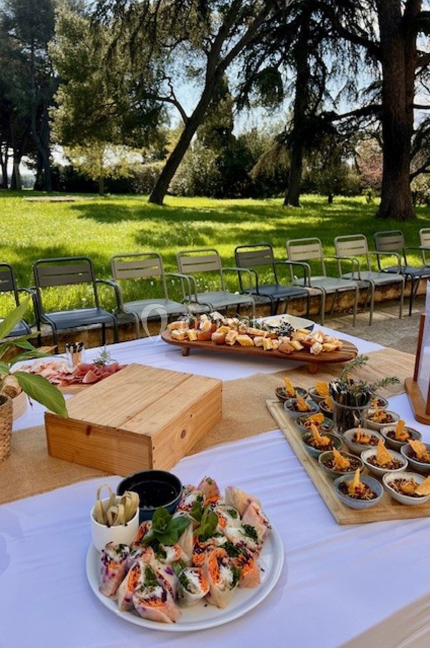 Table dressée en extérieur avec des plats variés, des rouleaux de printemps, des amuse-bouches et des chaises en arrière…