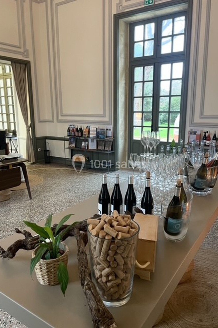Table avec bouteilles de vin, verres, bouchons en liège et décoration végétale dans une salle lumineuse avec grandes…