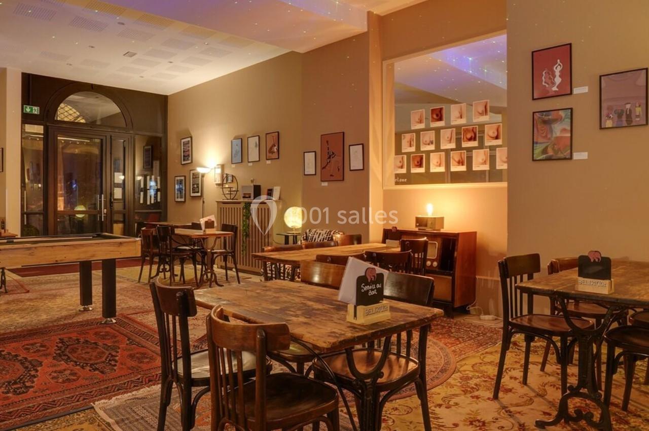 Salle chaleureuse avec tables en bois, tapis colorés, billard et murs décorés de cadres artistiques.