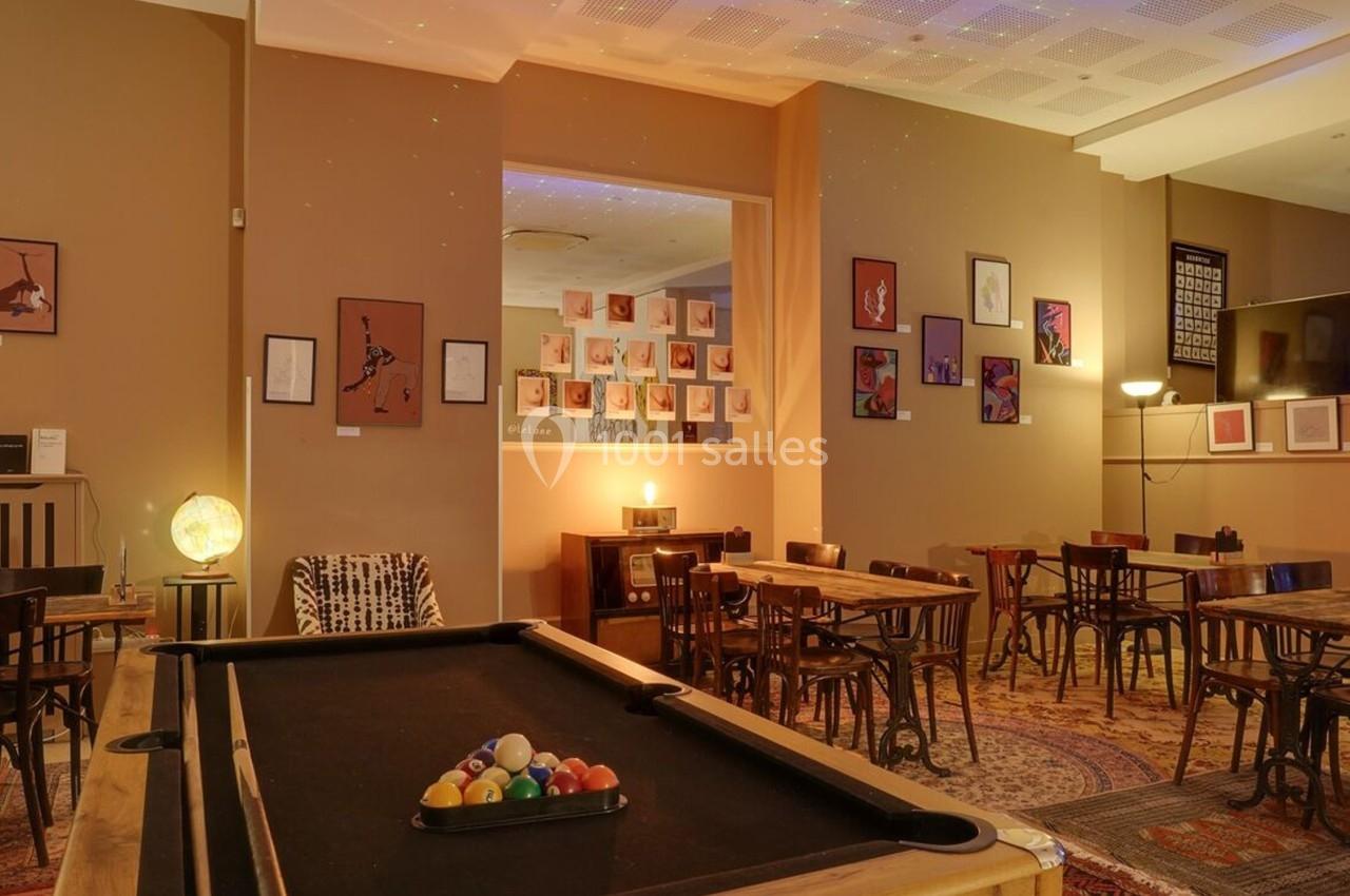 Salle conviviale avec tables en bois, billard au premier plan et décorations murales colorées.