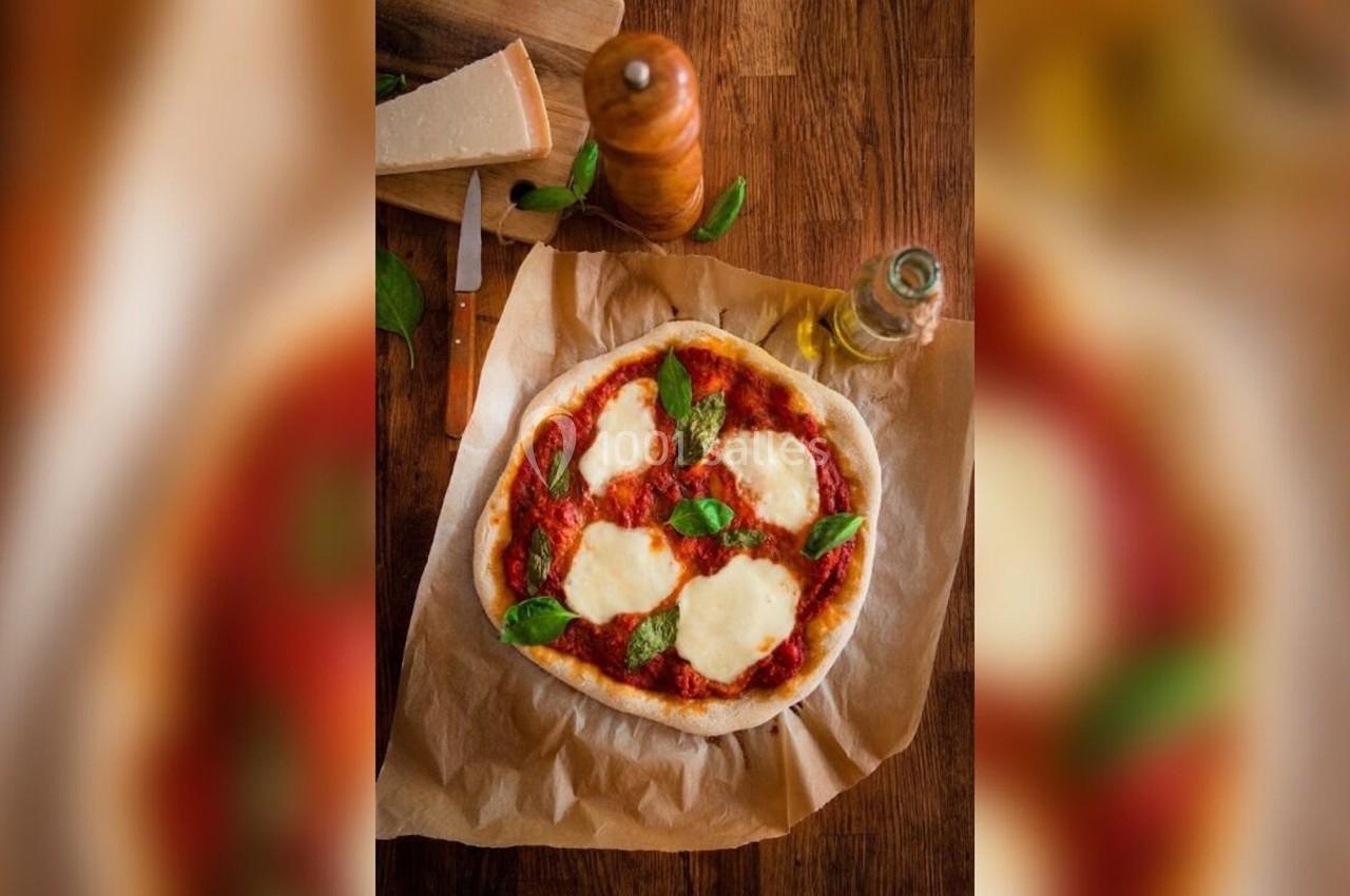 Pizza margherita sur papier cuisson, garnie de mozzarella fondue, feuilles de basilic et entourée d'ingrédients.