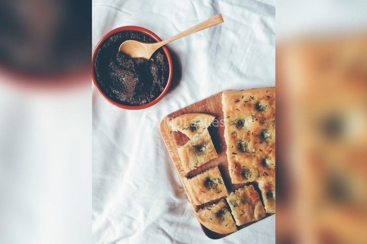 Focaccia coupée en morceaux sur une planche en bois, accompagnée d'un bol de tapenade et d'une cuillère en bois.