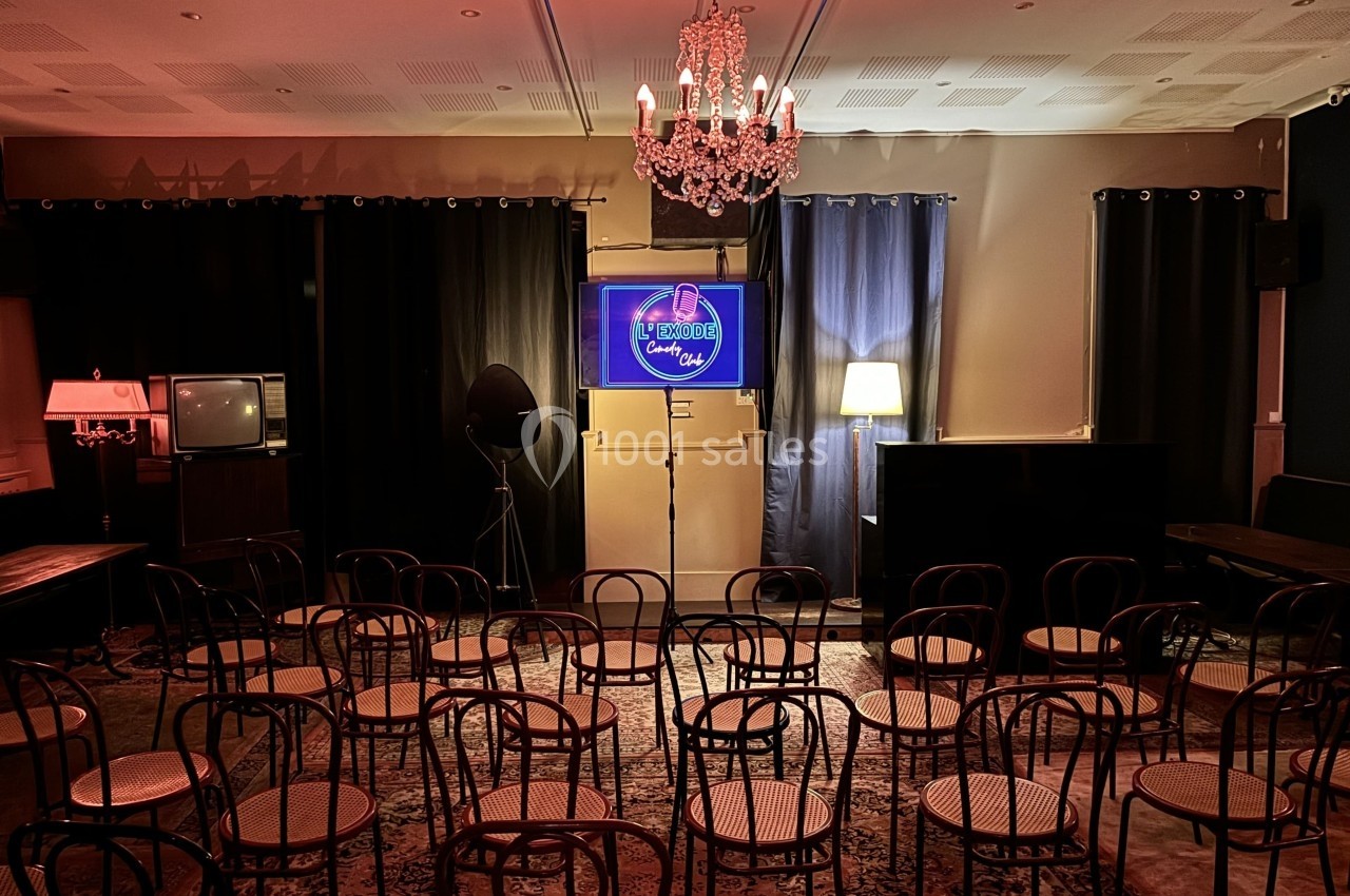 Salle avec des chaises disposées face à un écran lumineux sous un lustre, ambiance tamisée et rétro.