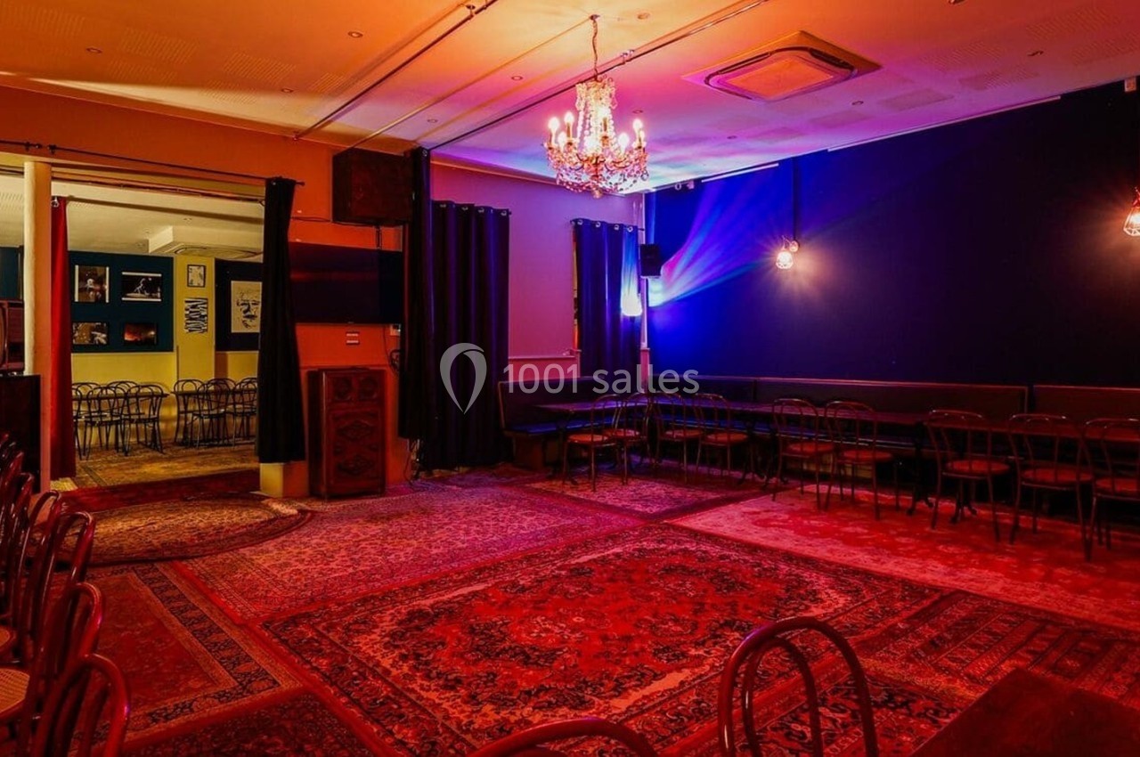 Salle avec tapis colorés, chaises alignées, murs sombres, éclairage tamisé et lustre central.