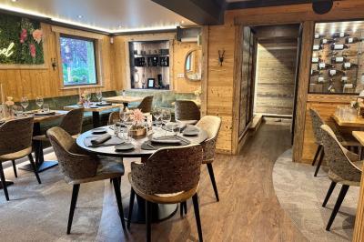 Bain à remous éclairé en violet sous une pergola en bois, avec un sapin décoré et un chalet en arrière-plan.