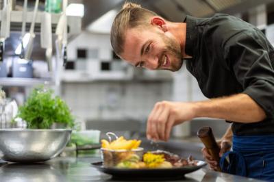 Bain à remous éclairé en violet sous une pergola en bois, avec un sapin décoré et un chalet en arrière-plan.
