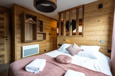 Bain à remous éclairé en violet sous une pergola en bois, avec un sapin décoré et un chalet en arrière-plan.