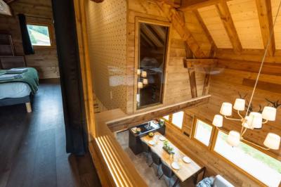 Bain à remous éclairé en violet sous une pergola en bois, avec un sapin décoré et un chalet en arrière-plan.