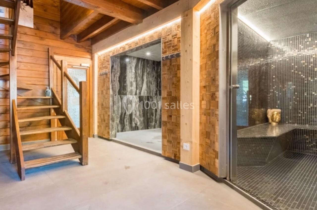 Escalier en bois menant à un étage, avec un espace détente comprenant un hammam et des murs en mosaïque et pierre.