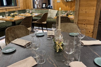 Bain à remous éclairé en violet sous une pergola en bois, avec un sapin décoré et un chalet en arrière-plan.
