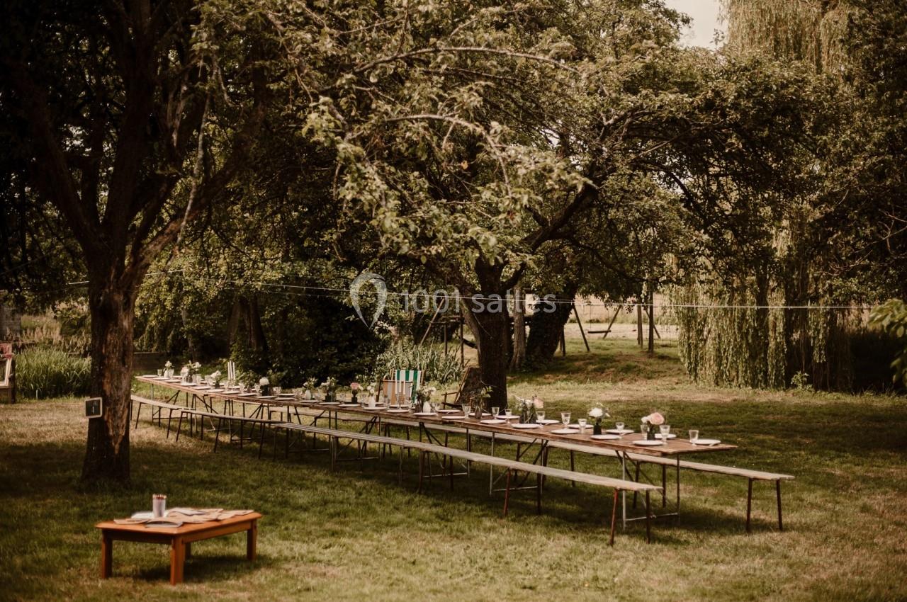Tables en bois disposées en extérieur sous des arbres, décorées pour un événement en plein air.