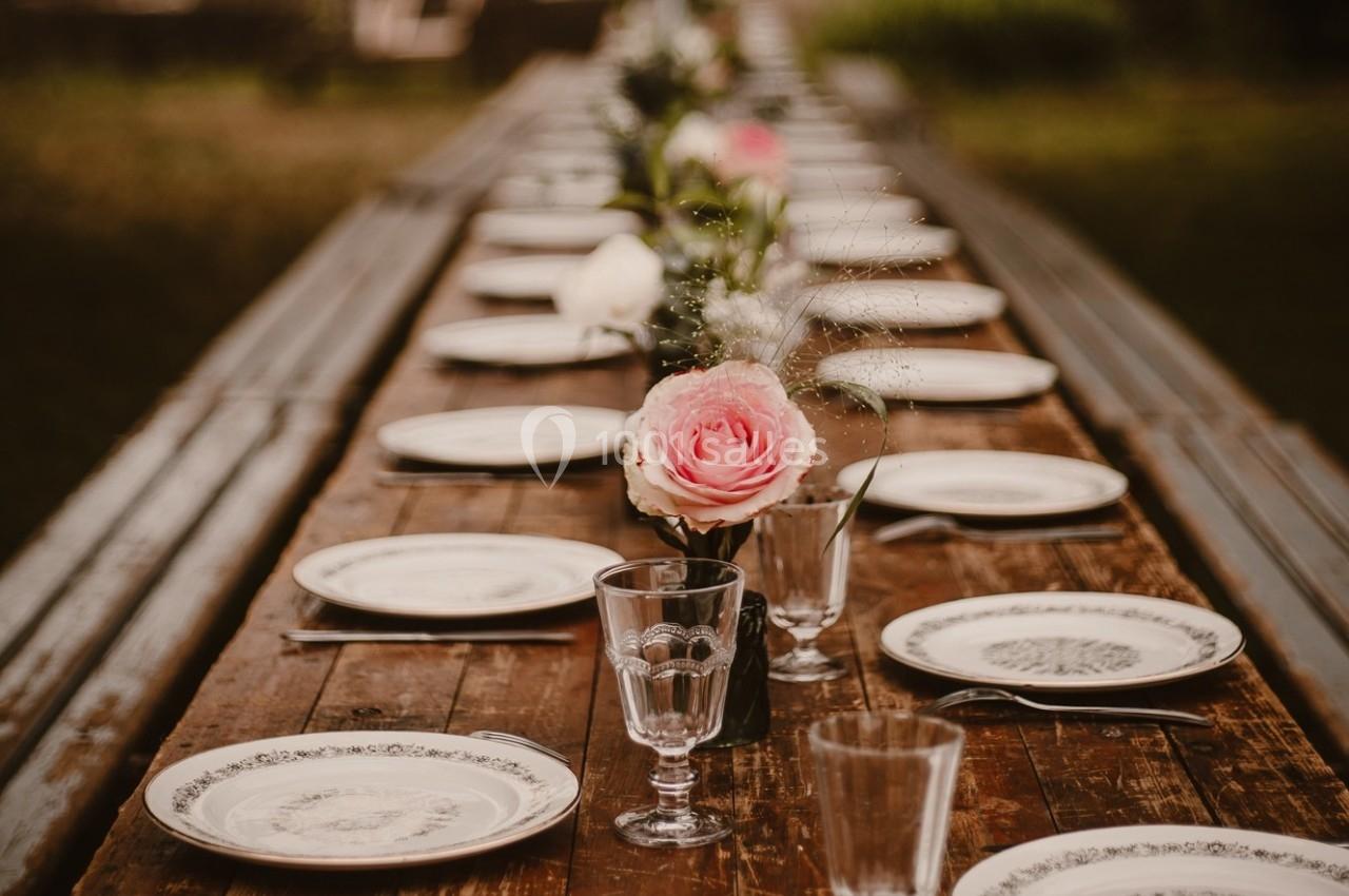 Table en bois dressée avec des assiettes blanches, des verres et des fleurs roses et blanches en centre de table.