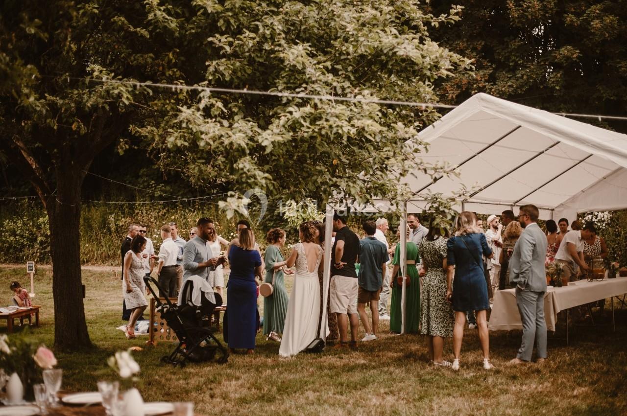 Groupe de personnes rassemblées sous une tente blanche dans un jardin lors d'un événement en plein air.