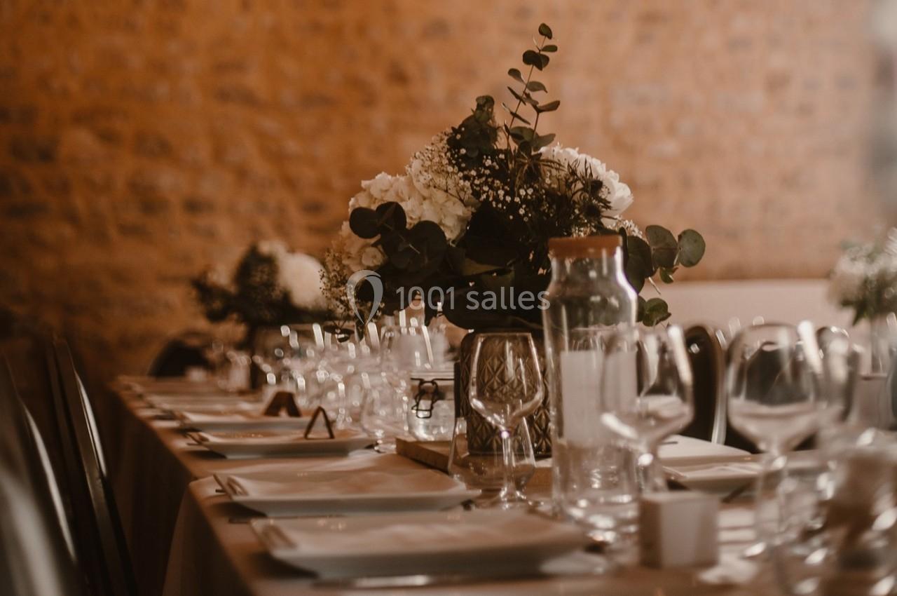 Table dressée avec vaisselle élégante, verres et centre de table floral dans une salle aux murs en pierre.