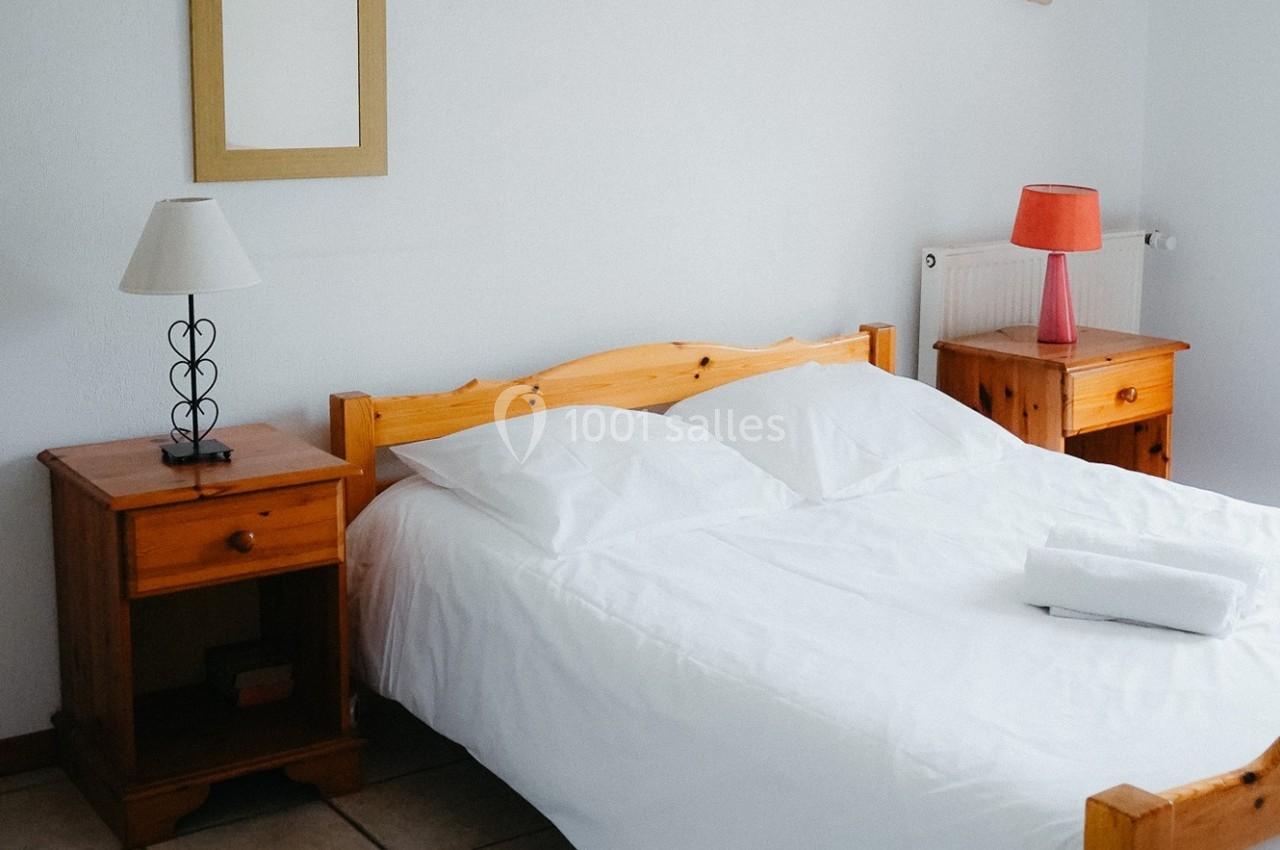 Lit double avec draps blancs, encadré par deux tables de chevet en bois, chacune avec une lampe.