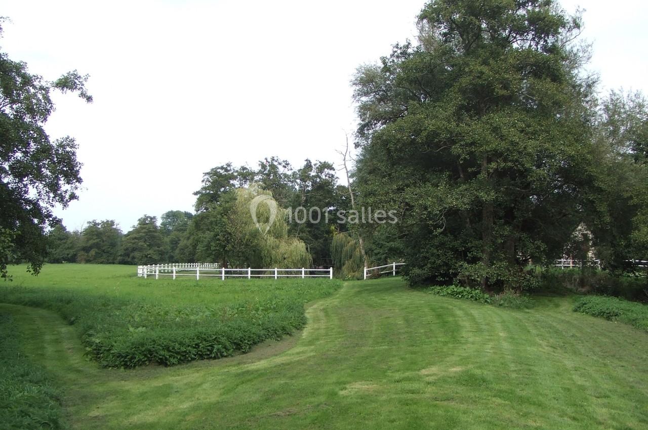Chemin herbeux menant à une clôture blanche entourée d'arbres et d'une prairie verdoyante.